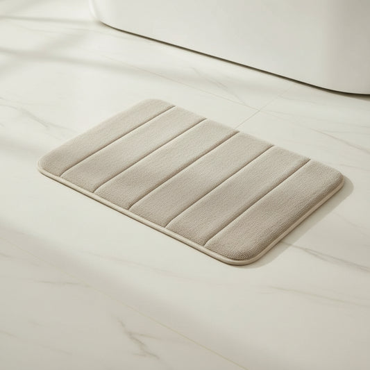 rectangular beige memory foam bath mat with ribbed texture placed on a bathroom floor near a bathtub
